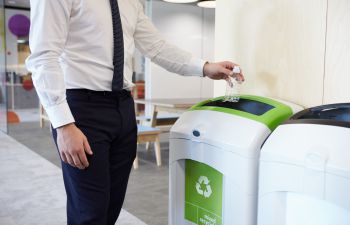 An employee in an office places a plastic bottle in the recycling bin