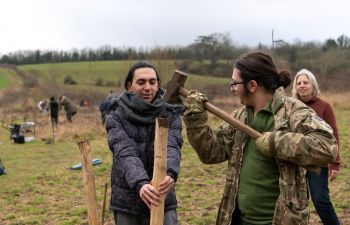 A student holds a large wooden stake as a staff volunteer raises a hammer to knock it into place