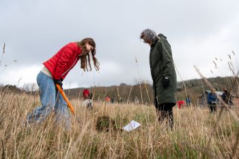 A student plunges a large spade into the ground while a staff volunteer looks on to learn