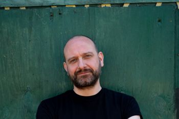 Keir Milburn (white man with beard wearing black t-shirt against a green background)