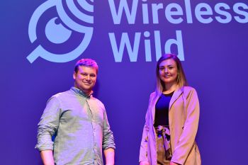 Two students stand on a drama stage with their company logo in the background