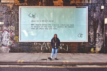 Zarina Muhammed standing in front of a large billboard promoting The White Pube and ideas for a new art world