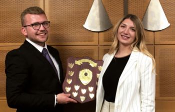 George Grammer-Taylor and Samantha Smith standing together, smiling holding shield in moot room