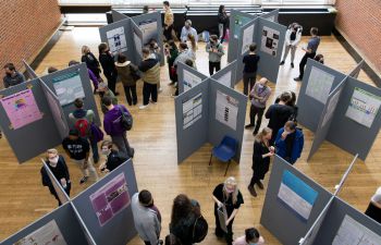 An overhead shot of the JRA posters exhibition showing academic posters on display boards, a crowd milling around them.