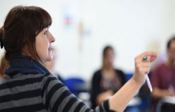 A female researchers teachers a training workshop at the front of a class of students.