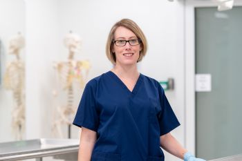 An image of prof Claire Smith smiling wearing blue scrubs in the anatomy room at Sussex