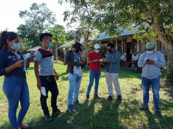 Six students standing next to each other outside on the grass in front of a building and wearing masks