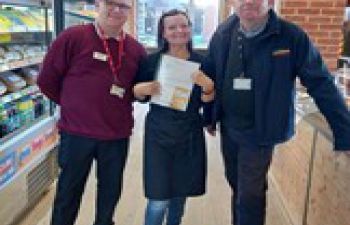 Woman on a black apron holding a certificate flanked by two taller men