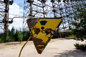 A faded and damaged yellow-and-black nuclear warning sign in the foreground on a disused nuclear plant site