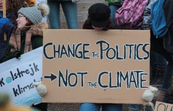 A person wearing a black hat and black coat stands in a protest holding up a cardboard placard