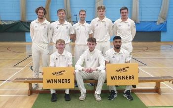 The cricket team in their white uniforms sitting on a bench and holding two yellow signs saying