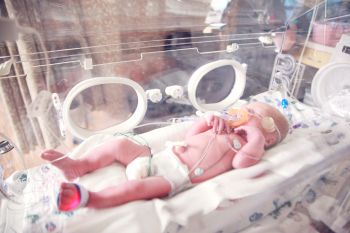 A premature baby lies in an incubator in a hospital connected to wires and breathing assistance