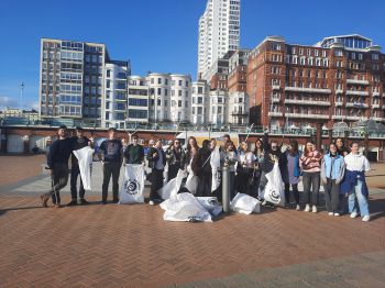 20 Volunteers stand together on the seafront holding litter pickers and white bags that have the Surfers against Sewage logo on them
