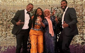 Four students wearing evening attire and smiling at the camera in front of a golden background