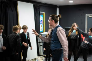 A male Sussex teacher trainee leads a drama class within his school placement setting