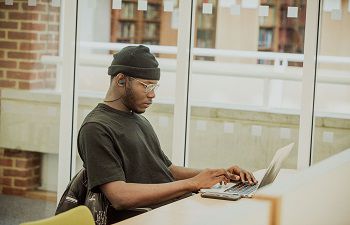A student sits at a library desk using a laptop