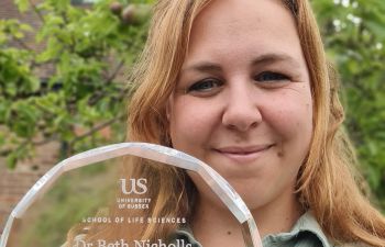 Beth Nicholls holding up the glass trophy for the Public Engagement Award