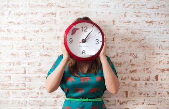 Woman holding a clock up to cover her face.