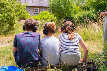 Young people are sitting on the grass wearing headphones and listening to sounds from 'a world never-before encountered' inside a tree with soundscape ecologist, Dr Alice Eldridge.