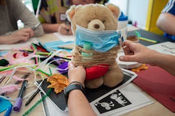 Hands are pictured that are attaching multiple objects to a tedd bear, including a hygiene mask, antibacterial hand gel and a lock, to highlight uncertainties of the time during the Covid-19 pandemic..