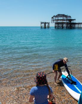 The ecologist Dr Mika Peck arrives on sunny Brighton beach on his standup paddle board. A child is pictured waiting by the shore.