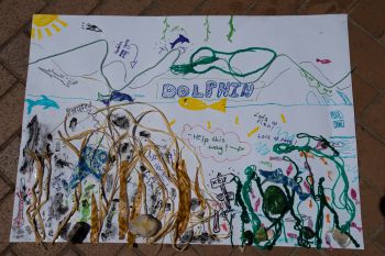 A children's colourful drawing picturing a partially biodiverse and partially polluted underwater world with kelp, algae dolphins, sharks and fish.