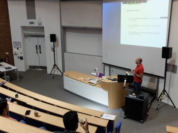 A PhD student presents their research at the front of a lecture theatre with an audience.