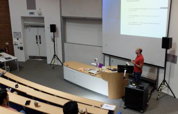 A PhD student presents their research at the front of a lecture theatre with an audience.