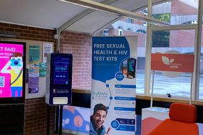 An image showing the new STI screen in a reception area next to a digital screen and a red chair