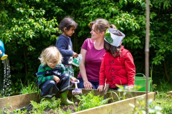 Lucy Owen-Collins sits at a raised bed with three young children at her forest kindergarten