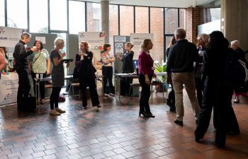 A group of people standing talking in a foyer with tiled floors and looking at mounted posters on boards