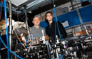 Founders of Sussex spin-out, Universal Quantum, Prof Winfried Hensinger and Dr Sebastian Weidt, standing behind the quantum computer that they built in their Sussex laboratory