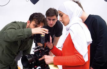 Four students (three male, one female) use a large video camera during a filmmaking teaching session