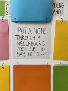 A note on a display board shows a suggested act of kindness by a Sussex student - it reads "Put a note through a neighbour's door just to say hello!"