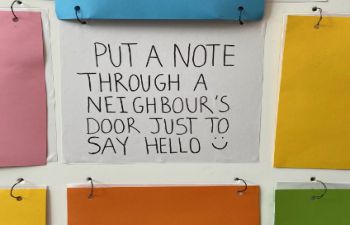A note on a display board shows a suggested act of kindness by a Sussex student - it reads "Put a note through a neighbour's door just to say hello!"