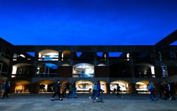 Students walk through Falmer courtyard at dusk, with one side of Falmer House in the background. Most of the windows are dark, with just a couple of rooms that have lights on.