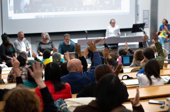 Back view of audience looking towards the panel. Audience members have hands raised