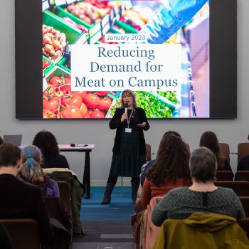 The Sustainability Manager, Sam Waugh, talks in front of an audience. The screen behind her shows a slide that reads 