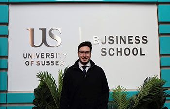 Alon Sammy - Final Year BSc Finance student stood in front of the Business School logo