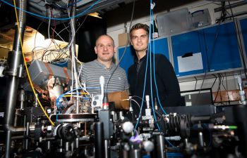 Professor Winfried Hensinger and Dr Sebastian Weidt behind a prototype of a quantum computer in the University of Sussex quantum lab