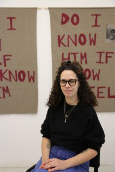 A photo of Jamila Prowse seated with a sign behind.