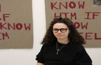 A photo of Jamila Prowse seated with a sign behind.