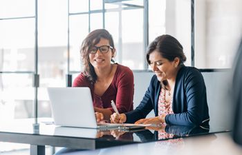 Two women sat next to each other in front of a laptop