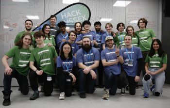The HackSussex team are shown smiling together with the HackSussex flag in the Future Technologies Lab.