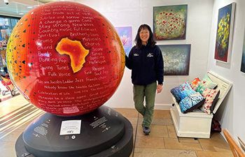 Local artist Serena Sussex standing with her globe design named ‘The Inner Voice Through Music’