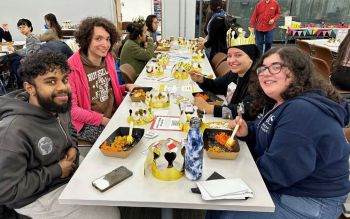 students eating together at a table decorated with golden cardboard crowns and smiling at the camera