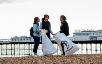 Two students speaking with Kelly Coate near the Palace Pier during a beach clean