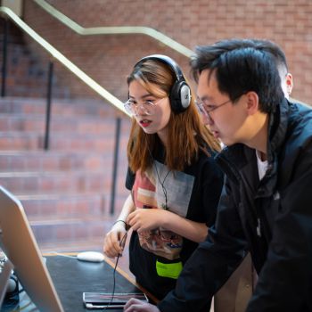 Two students wearing headphones interact with a screen.