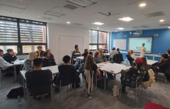 Class room of students listening to a speaker standing at the front of the room