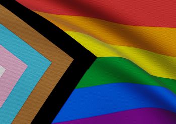 A close up of the progress pride rainbow flag which includes stripes in the trans pride colours and black and brown stripes.